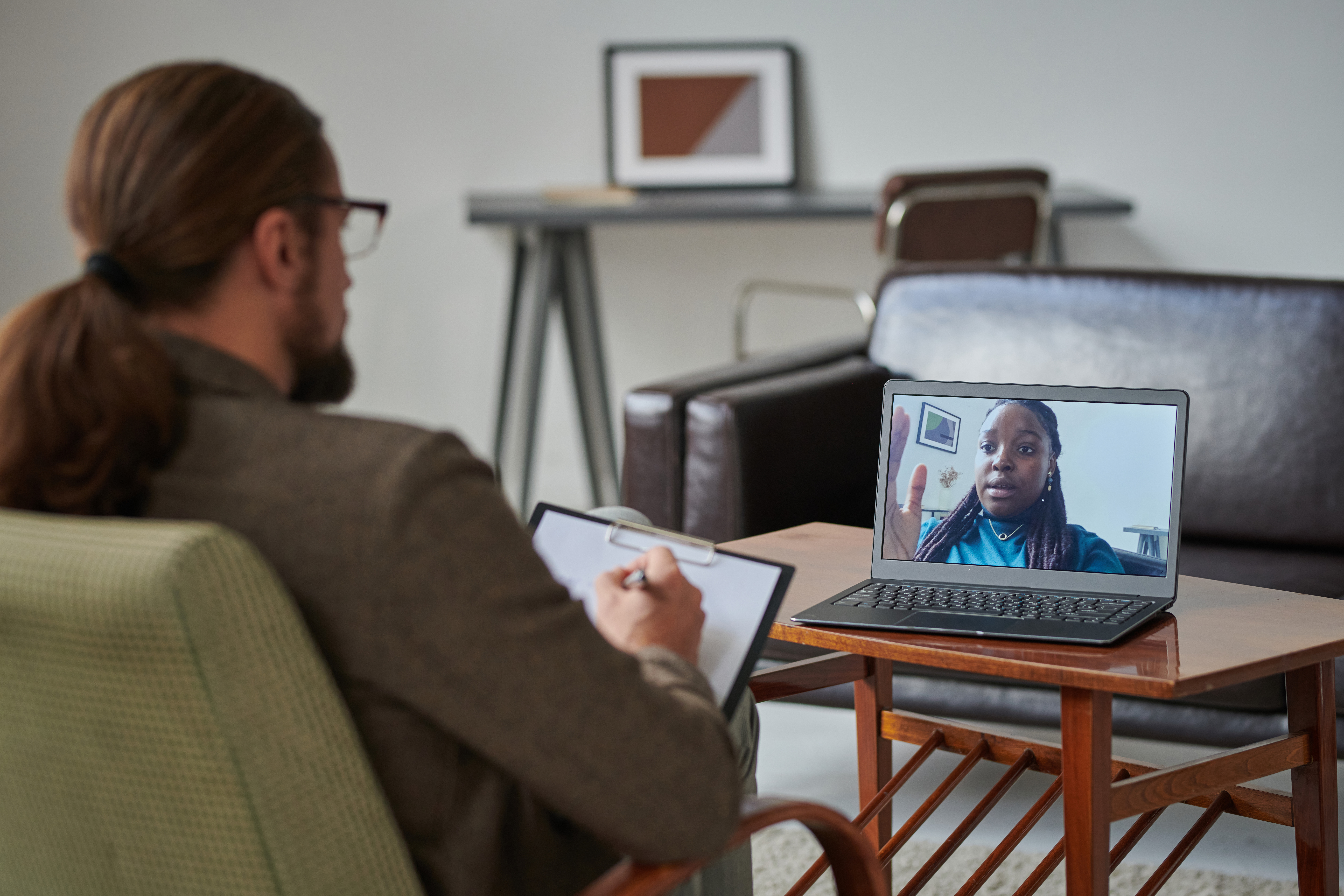 African American young girl talking to psychologist online, she discussing problems while he making notes in card